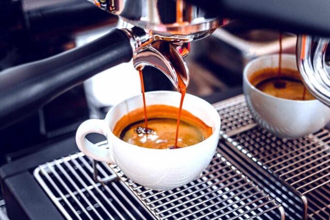 A café cup on an espresso machine with espresso being brewed into it