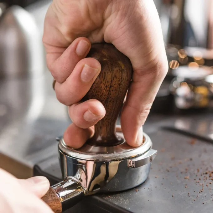 A hand using a tamper to tamp espresso down in a portafilter